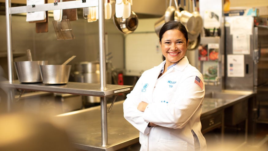 Worker in an Ecolab lab coat standing in a professional kitchen with arms crossed