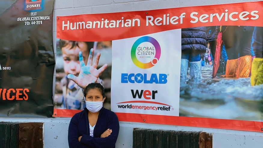 Masked woman standing next to a World Emergency Relief Services banner