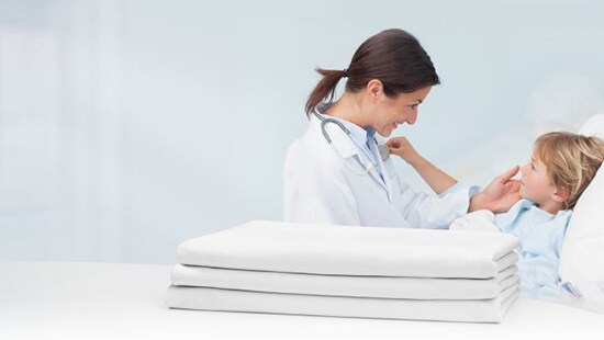 Healthcare professional looking after a young boy resting on a bed with fresh hospital laundry on a table.