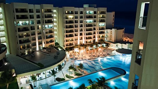 Large hotel at night overlooking a large pool and patio.